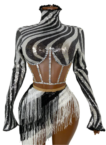Mannequin wearing a zebra print sequin top and white fringe skirt against a white wall.
